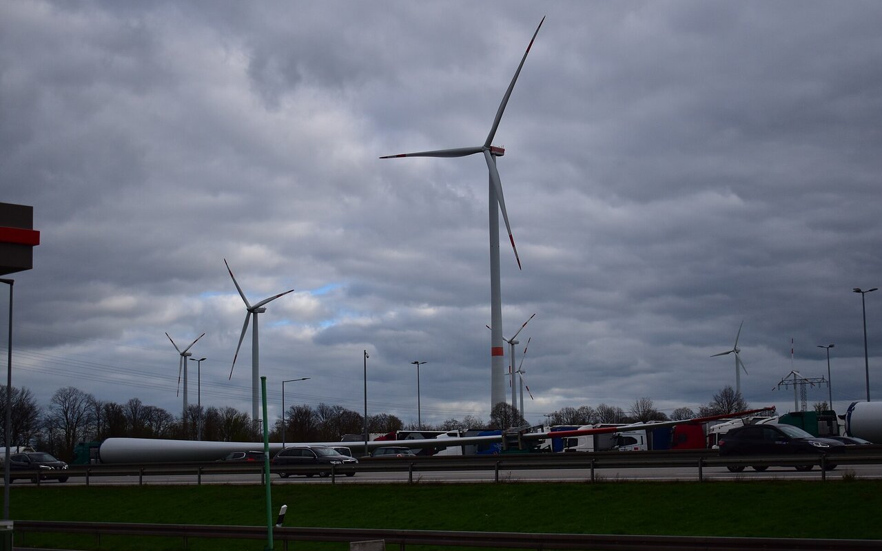 Pale de rotor d'éolienne géante sur un parking autoroutier, comparée en taille avec des camions