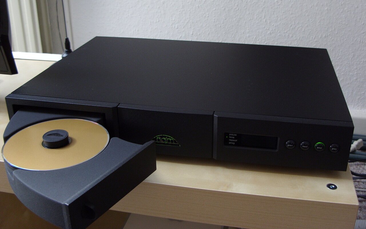 Lecteur de disques compacts Naim Audio CD5 posé sur un meuble, façade ouverte laissant voir le plateau et le presseur de disque