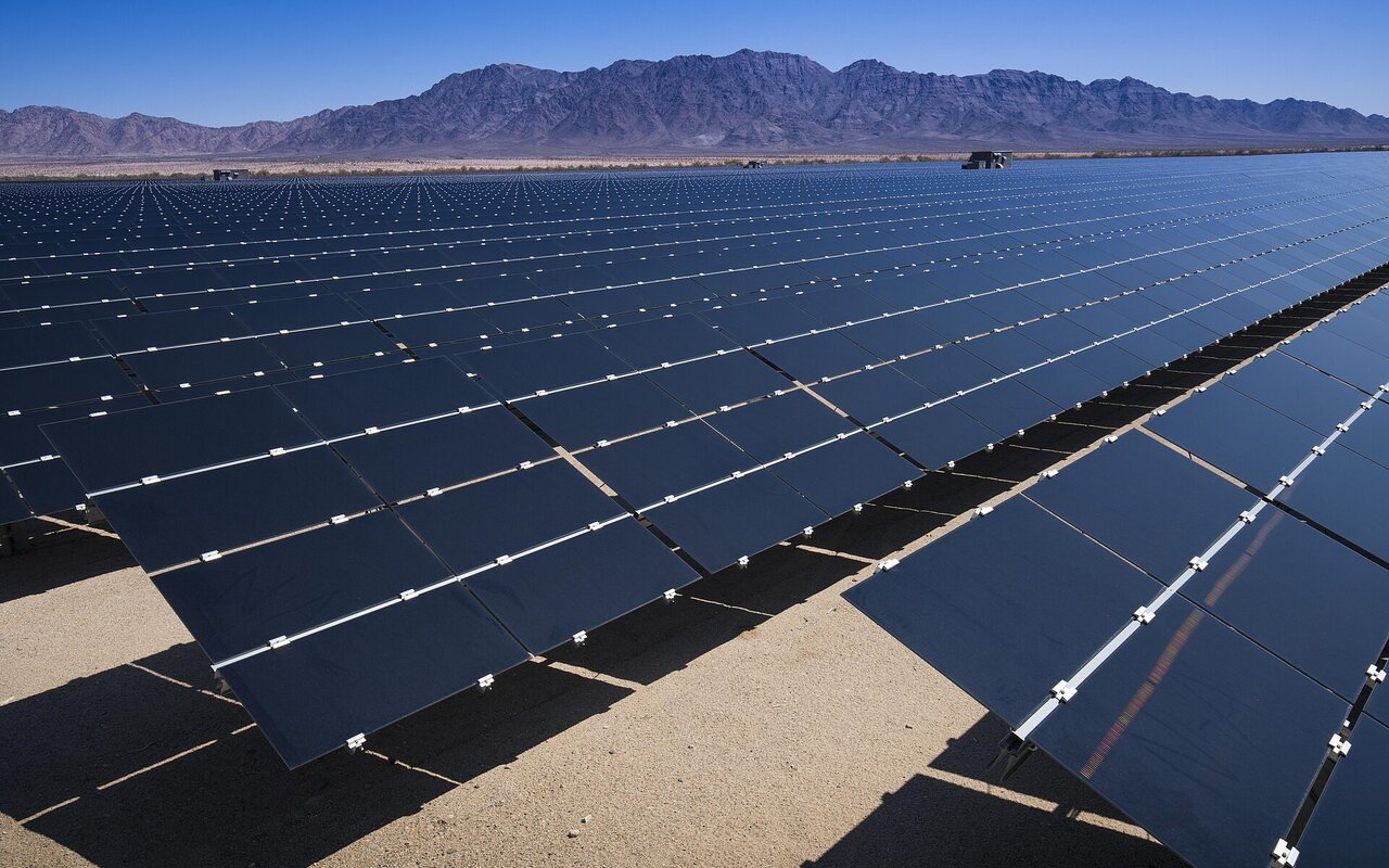 Longues rangées de panneaux photovoltaïques d'une centrale solaire dans le désert californien, montagnes en arrière-plan