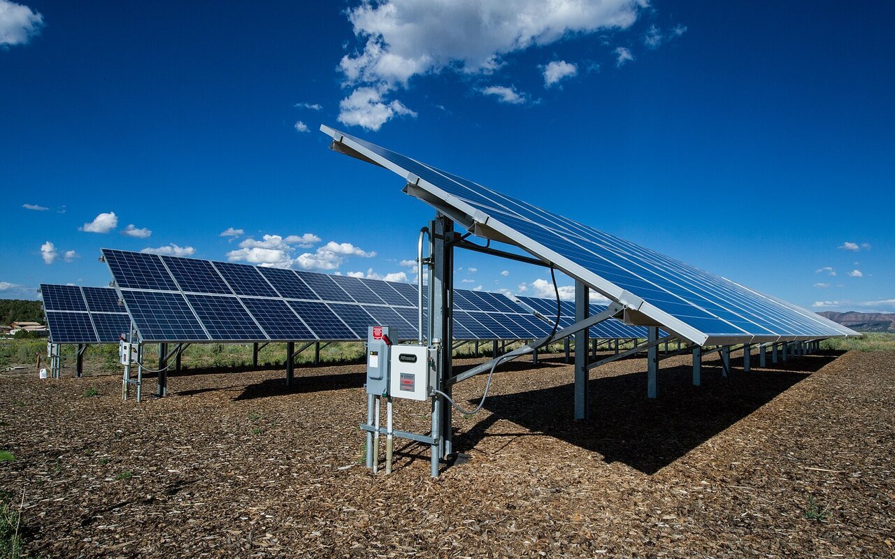Rangées de panneaux photovoltaïques montés sur des structures inclinées dans un paysage désertique, sous un ciel bleu