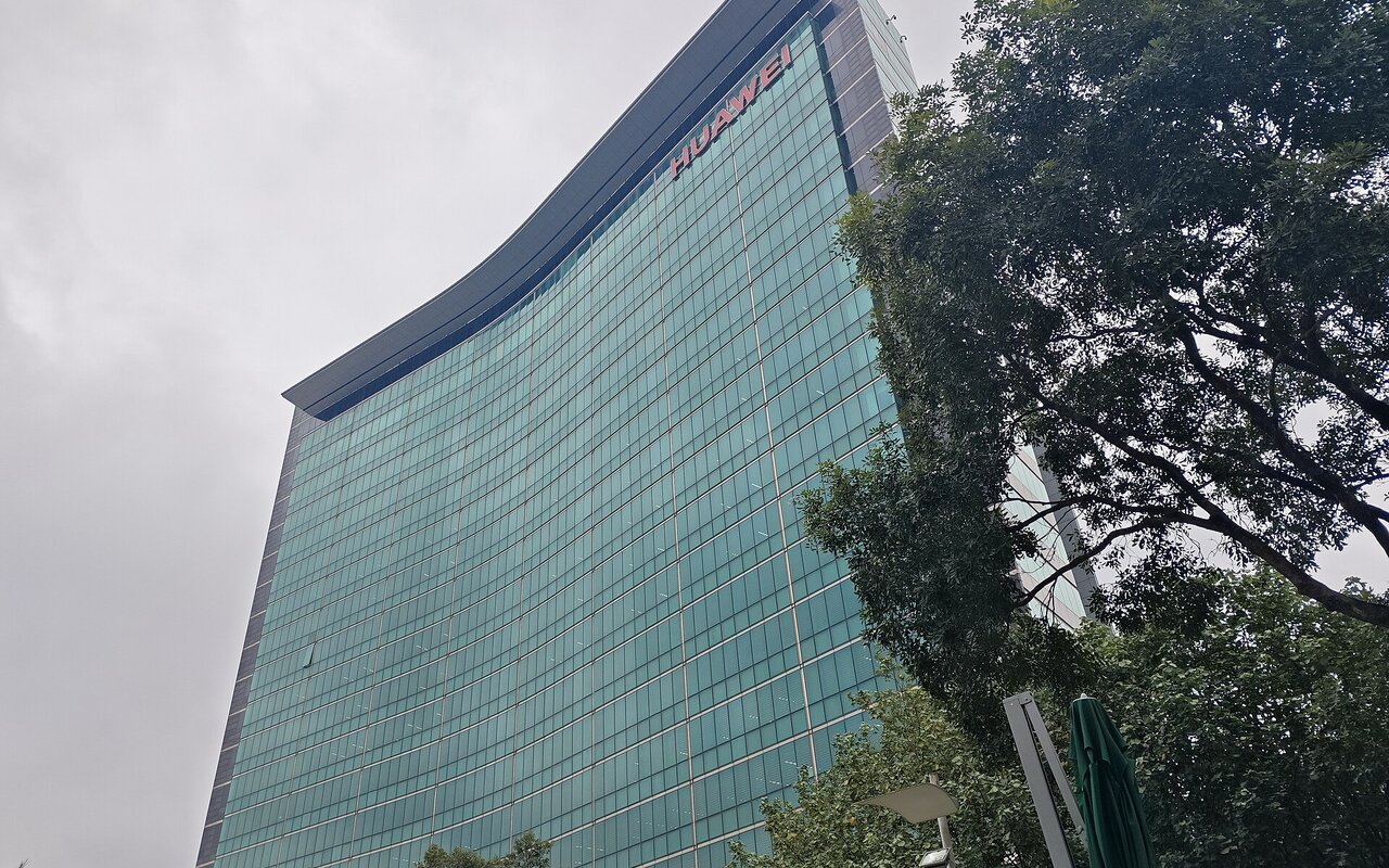 Vue en contre-plongée d'une tour de bureaux en verre portant le nom Huawei sur sa façade, sous un ciel gris