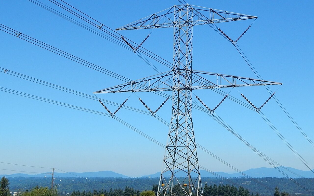 Pylône métallique de transport d'électricité à haute tension portant plusieurs faisceaux de conducteurs, photographié en contre-plongée sous un ciel bleu, avec des collines à l'arrière-plan