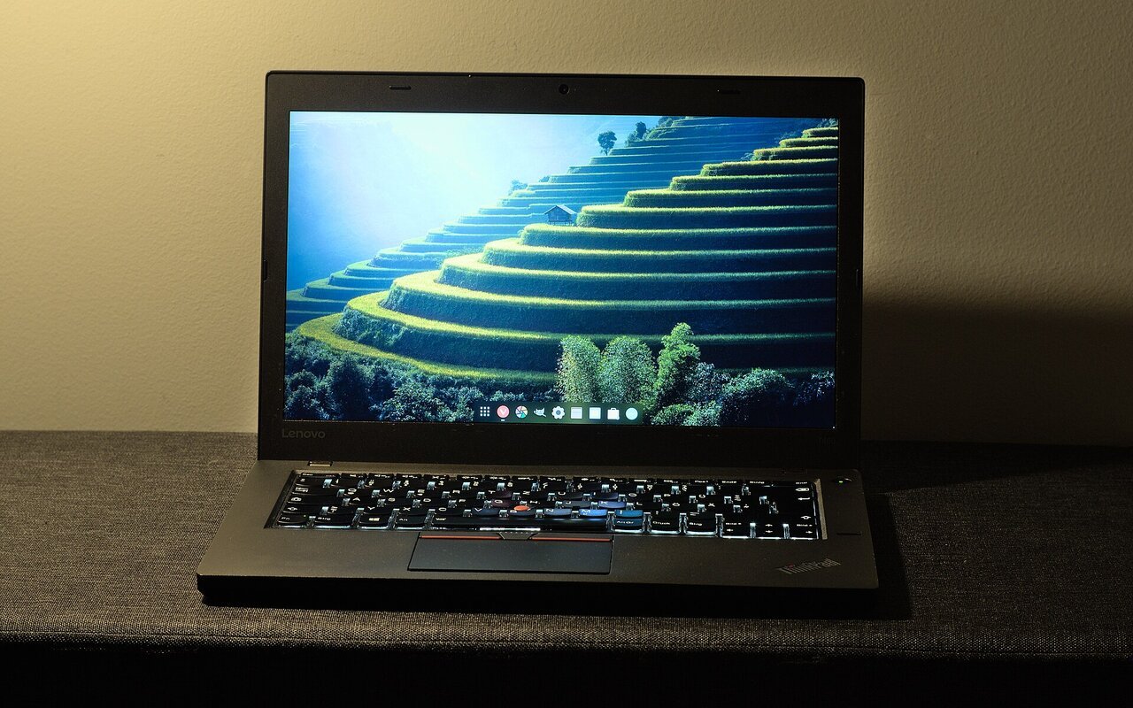 Ordinateur portable professionnel noir, ouvert sur une table, affichant un environnement de bureau Linux avec une barre d'icônes en bas de l'écran