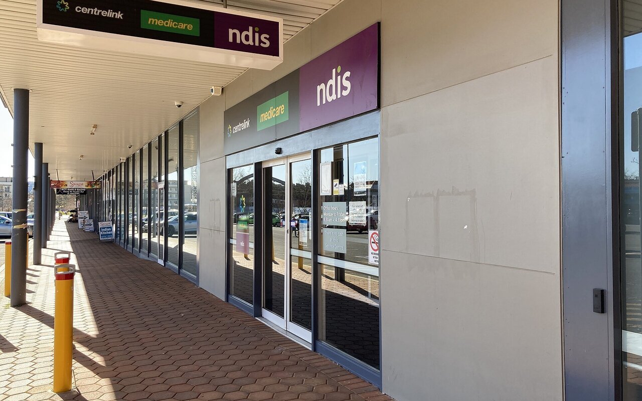 Entrée vitrée d'un centre de services de Services Australia à Tuggeranong, avec les enseignes de plusieurs services publics australiens au-dessus de la porte