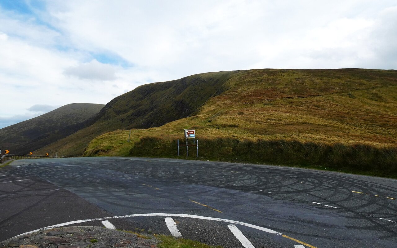 Marques de pneus sur une route asphaltée grise près d'un parking en montagne.