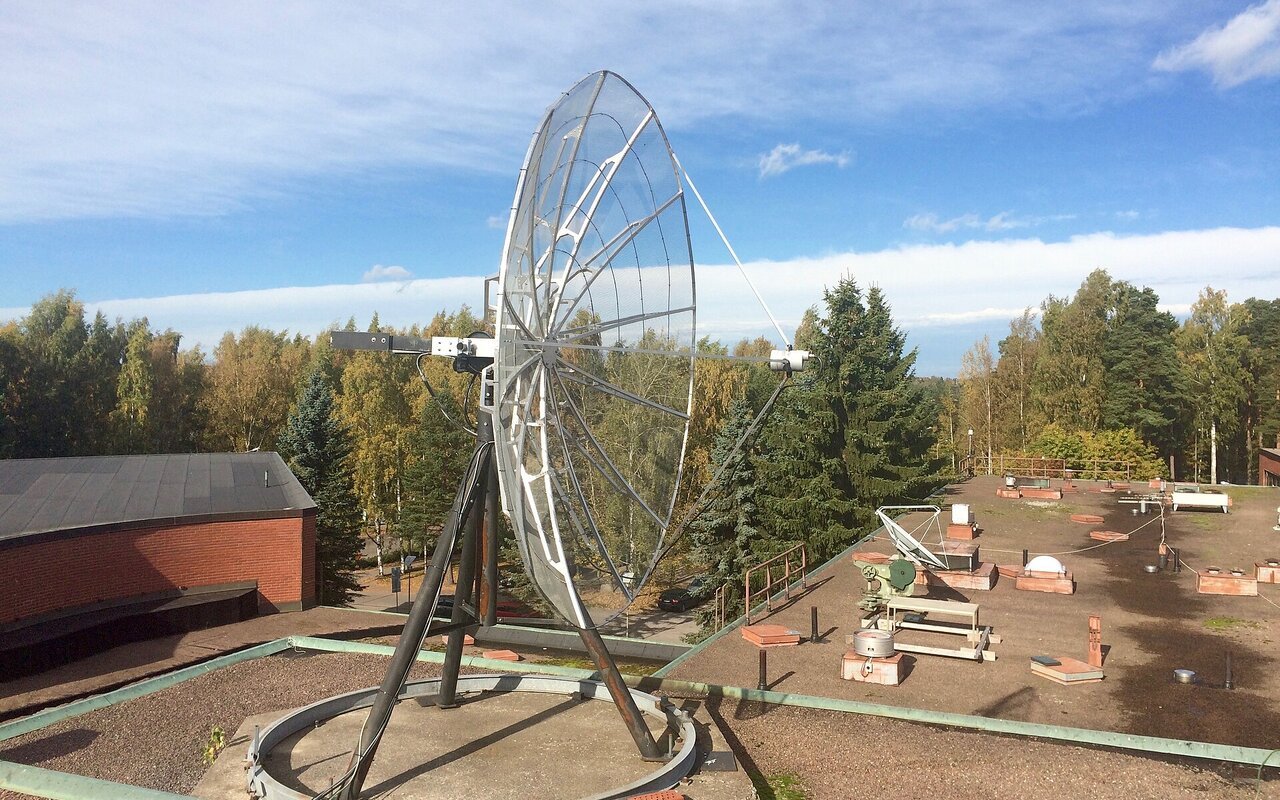 Antenne parabolique blanche montée sur une structure métallique, utilisée comme station de réception au sol.