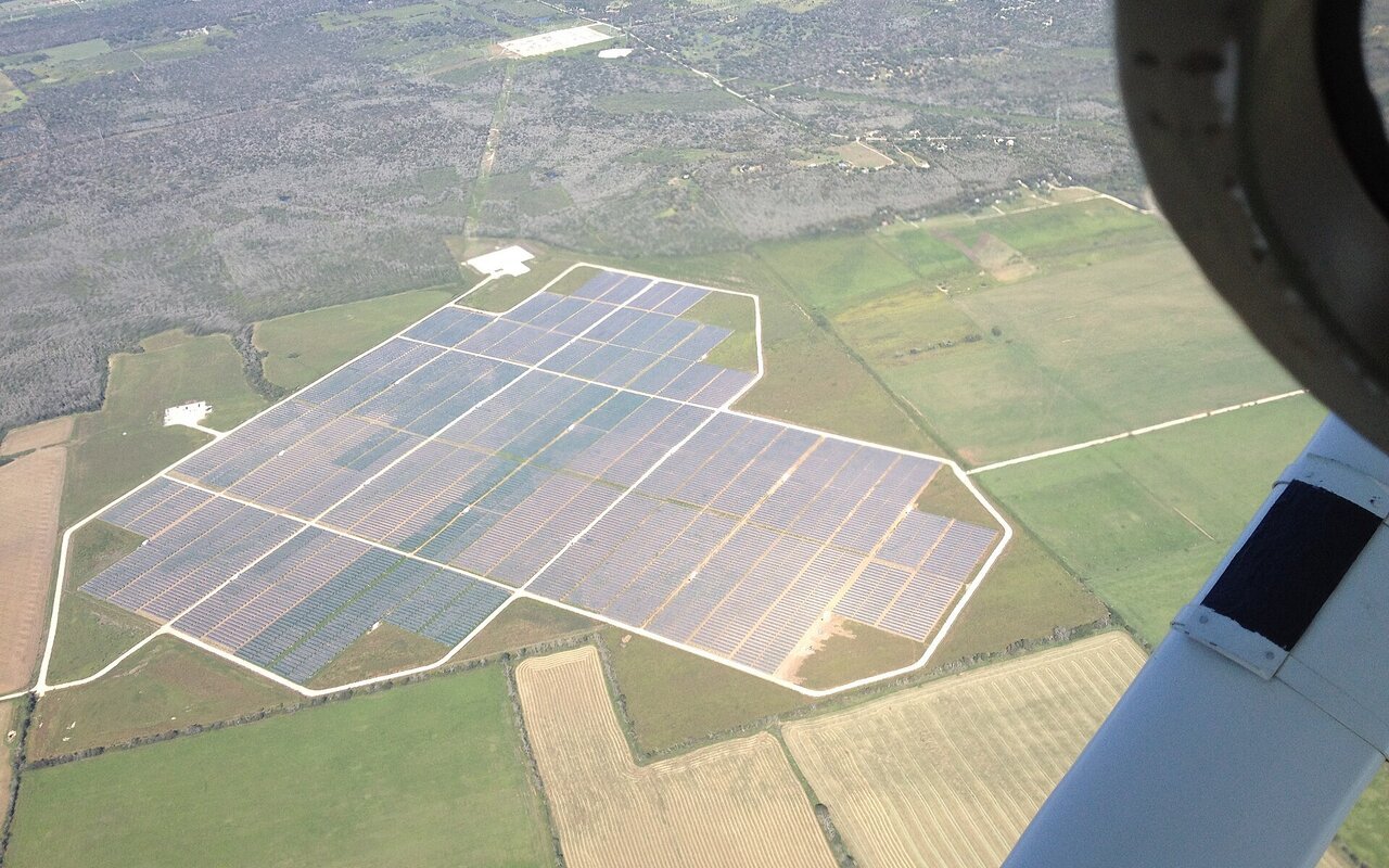 Vue aérienne d'une grande ferme solaire avec nombreux panneaux photovoltaïques alignés au sol.