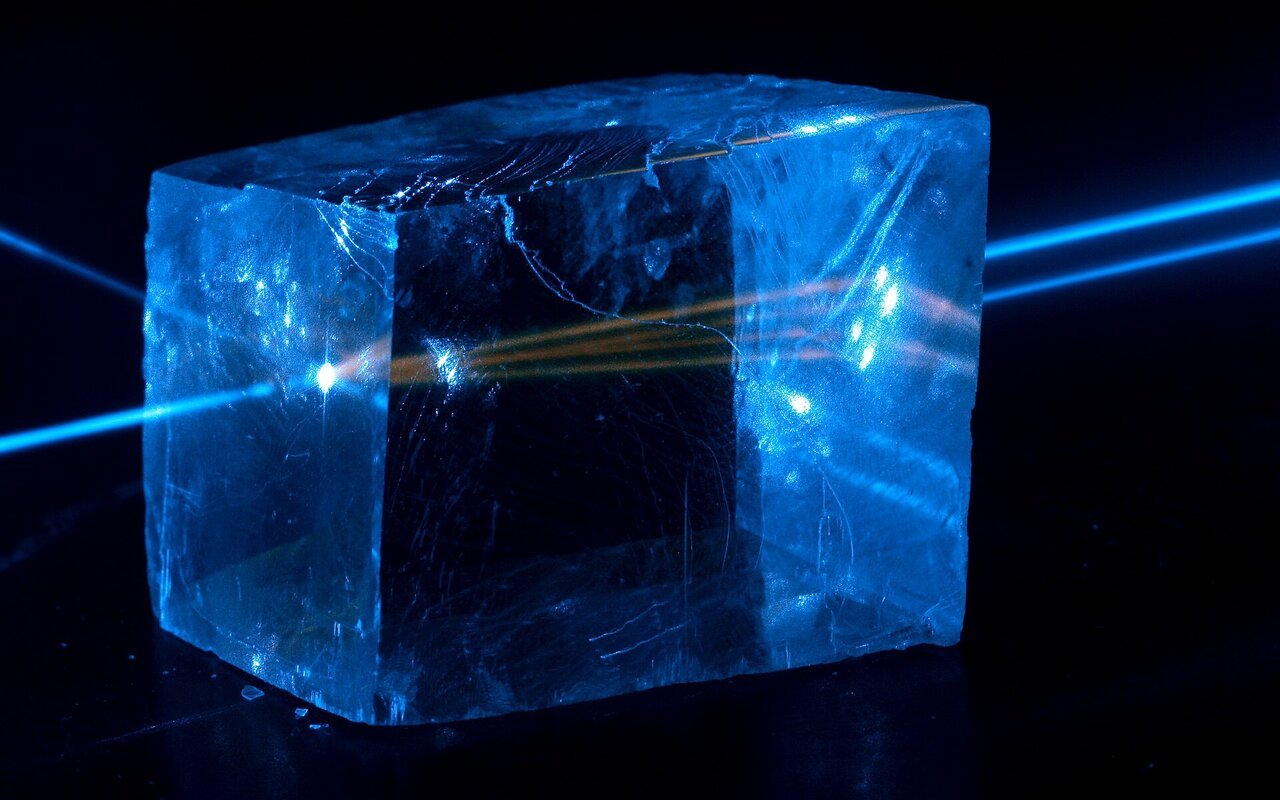 Faisceau laser bleu traversant un cristal de calcite avec fluorescence visible