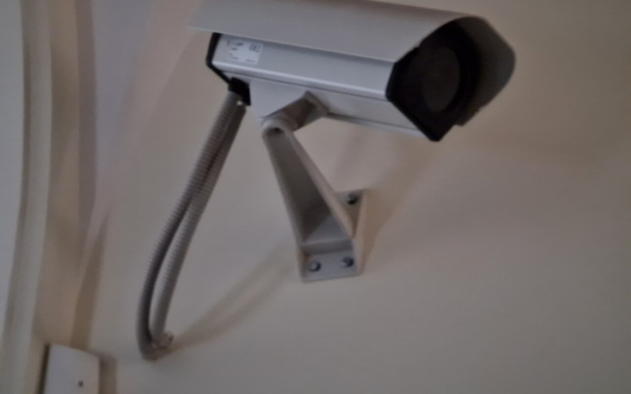 Caméra de surveillance CCTV montée sur un mur blanc, avec boîtier blanc et lentille noire visible.