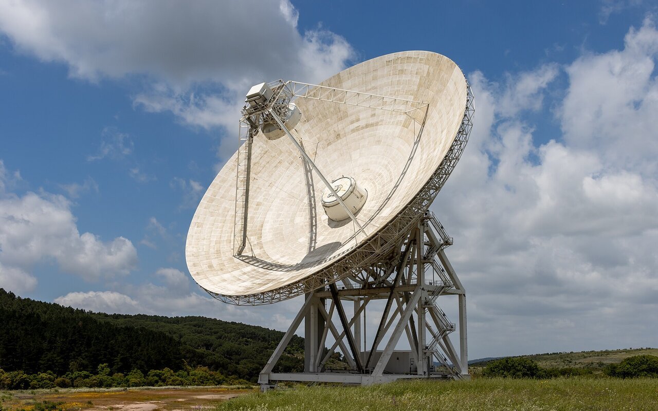 Grand radiotélescope parabolique blanc en Sardaigne, structure massive de recherche astronomique en zone désertique.