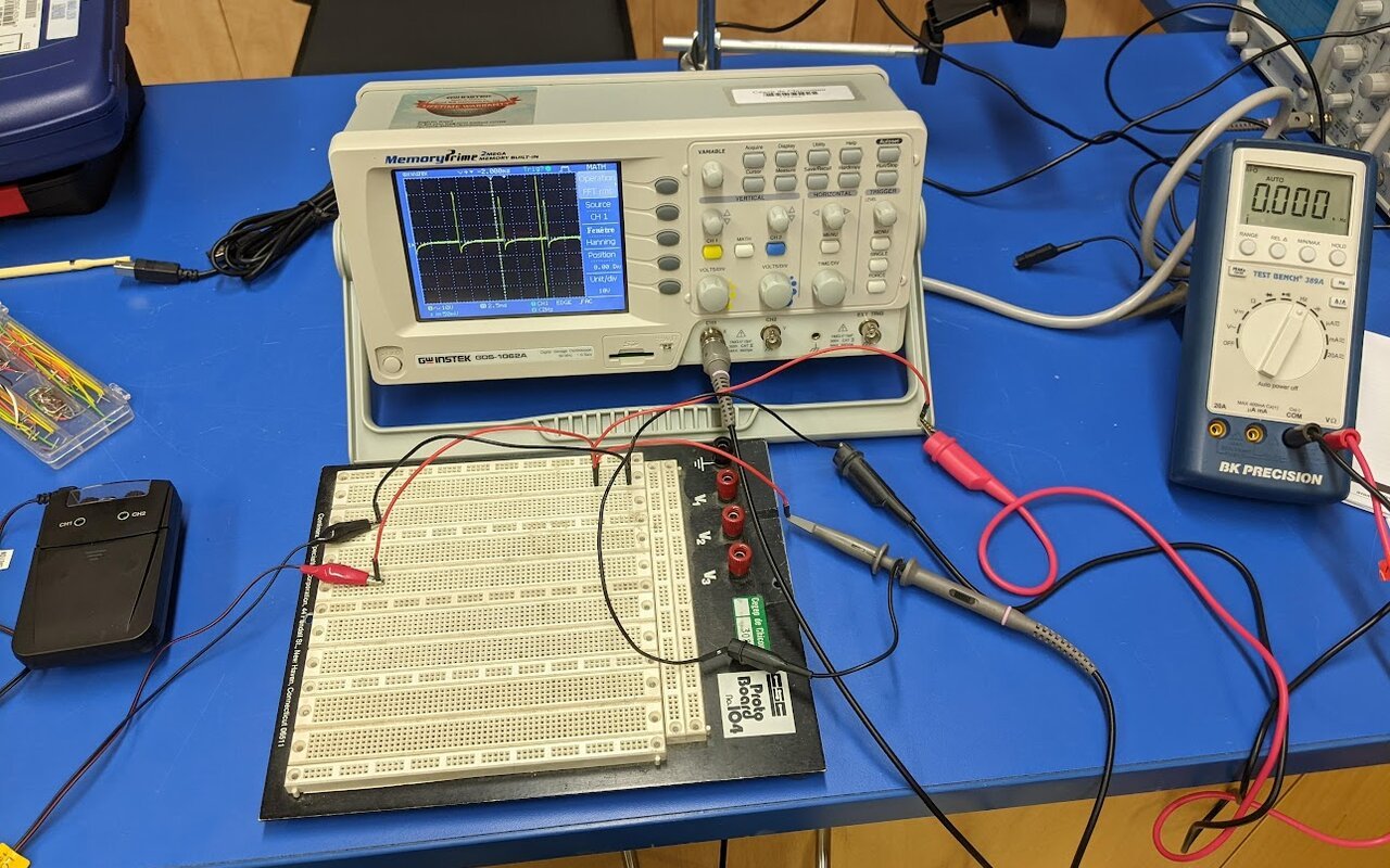 Un appareil TENS connecté via des câbles à un oscilloscope numérique et un multimètre pour mesure de signal.