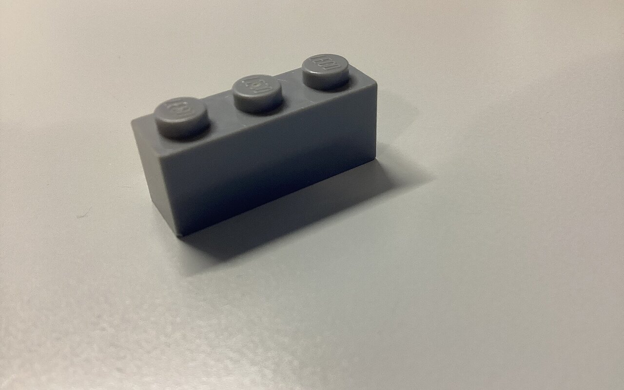 Une brique Lego grise 1x3 isolée sur fond blanc