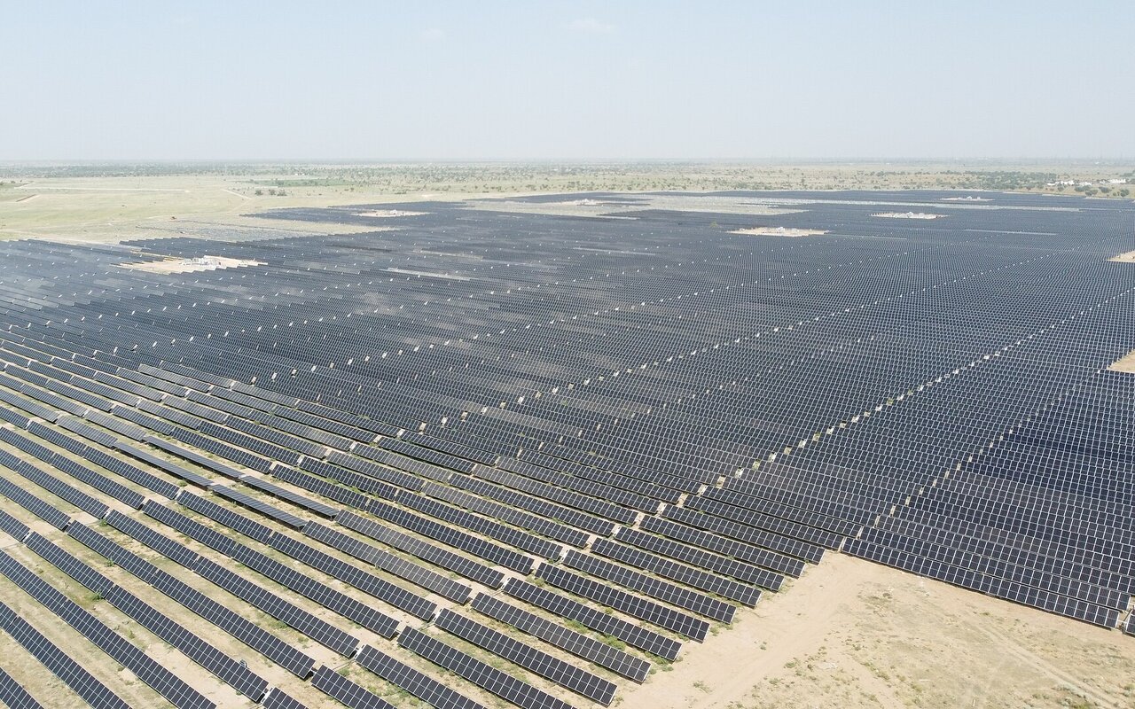 Vaste centrale solaire avec des milliers de panneaux photovoltaïques alignés en rangées régulières.