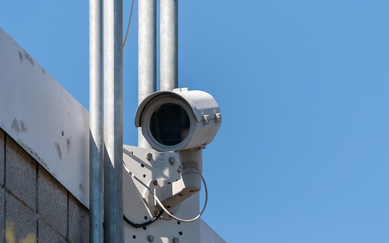 Caméra de surveillance montée sur un poteau, vue de face, avec boîtier blanc et dôme transparent.