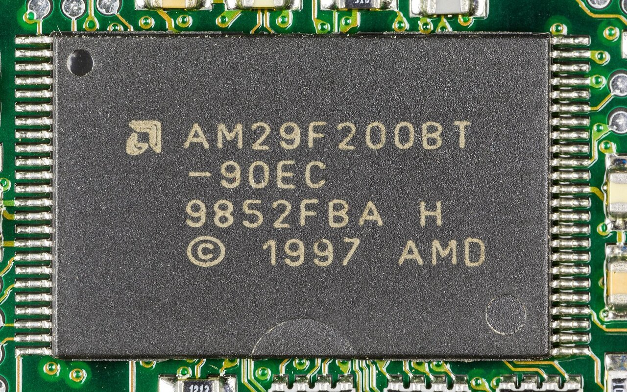 Gros plan d'une puce de mémoire flash NOR AMD AM29F200BT soudée sur un circuit imprimé vert d'un équipement réseau 3COM