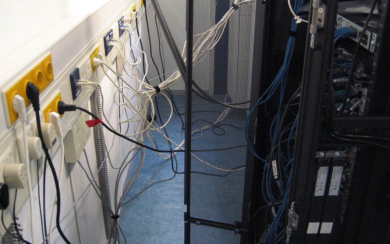 Serveur IBM entouré de câbles enchevêtrés et mal organisés derrière des baies de serveurs.