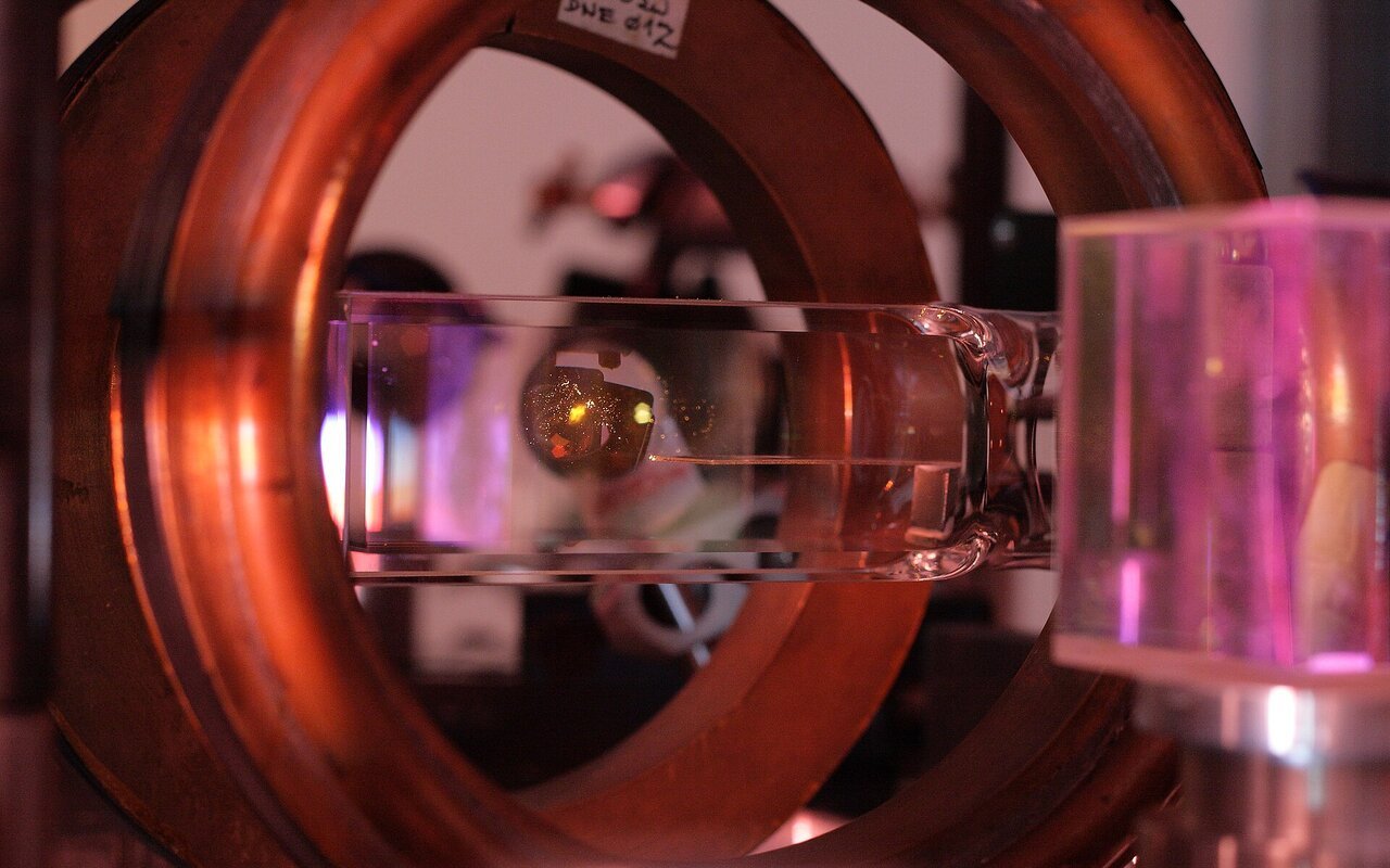 Chambre à vide en verre contenant un nuage jaune-orange d'atomes refroidis