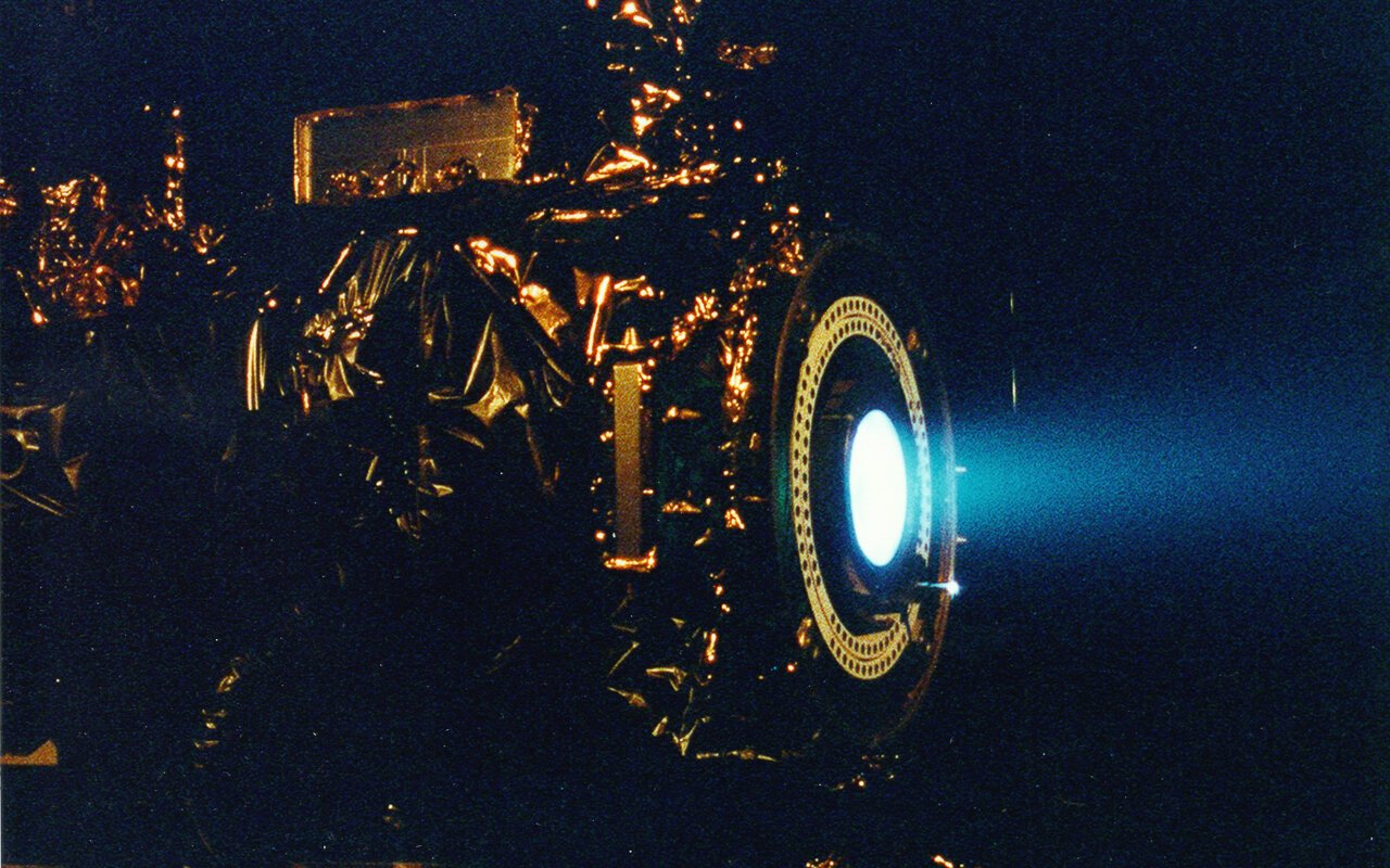 Moteur à ions au xénon en test dans une chambre à vide, montrant le faisceau ionique bleuté caractéristique
