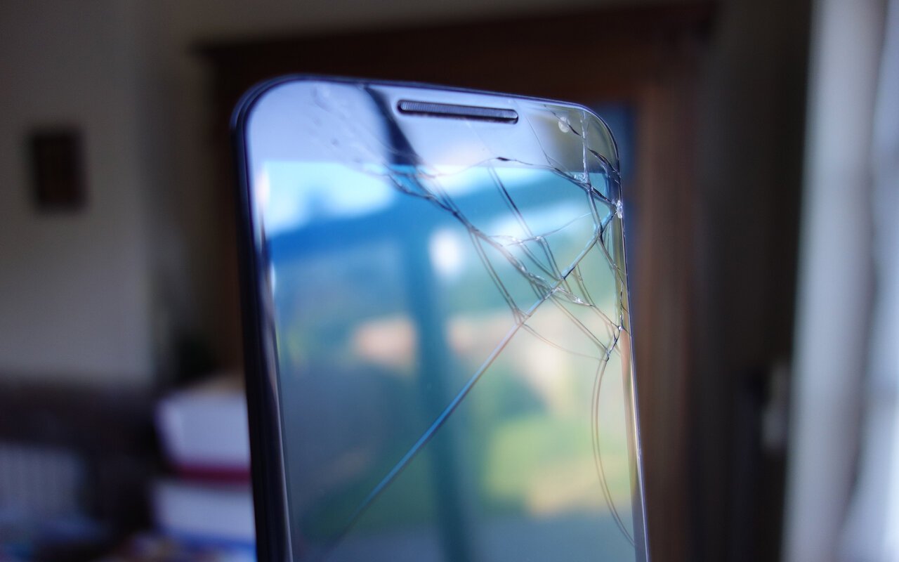 Écran de smartphone fissuré reflétant un jardin
