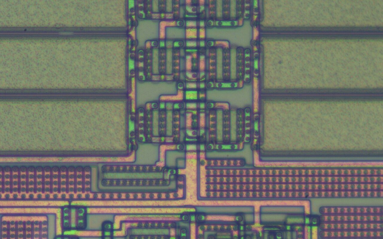 Photomicrographie en couleurs d'une puce électronique décapsulée, montrant les pistes métalliques et les zones de circuit gravées dans le silicium