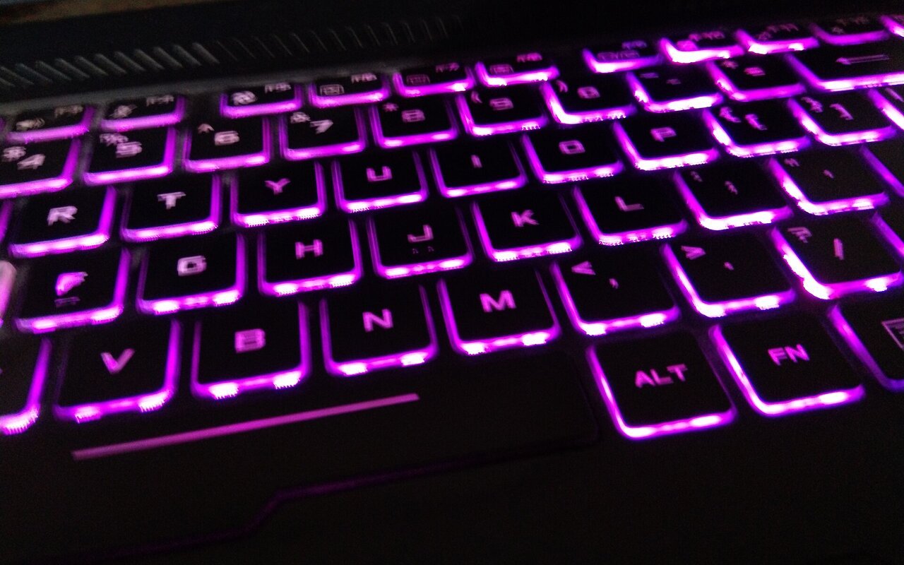 Clavier d'ordinateur rétroéclairé avec des touches illuminées en bleu, photographié en contre-jour.