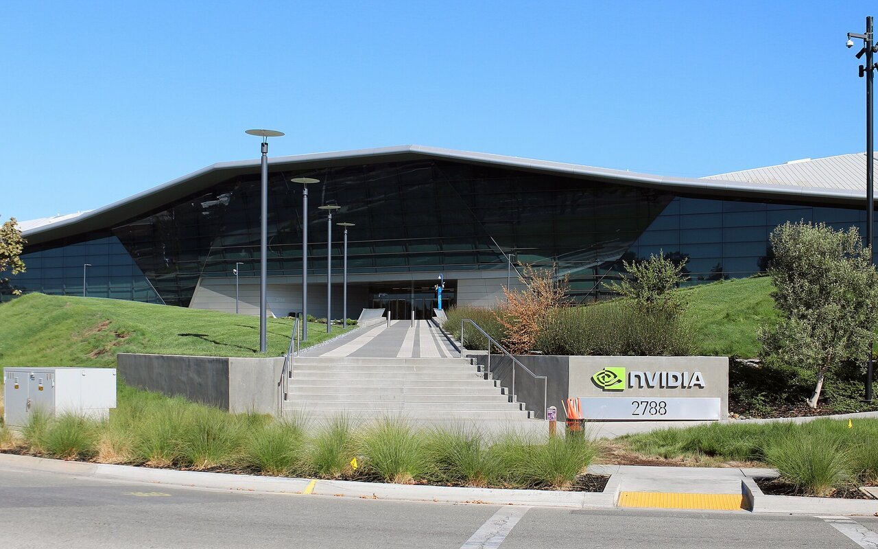 Le bâtiment du siège de Nvidia à Santa Clara, avec son logo vert devant l'entrée et un ciel bleu.