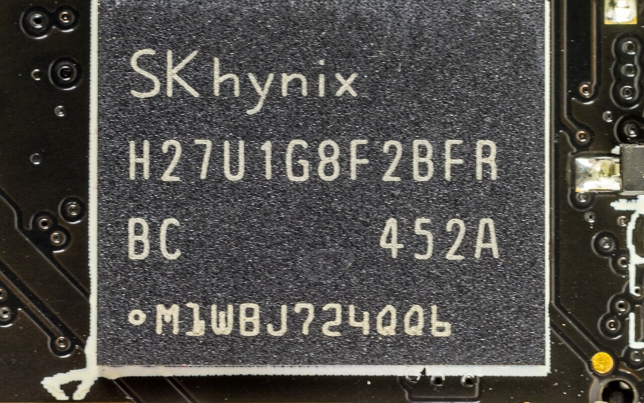Gros plan sur une puce de mémoire flash NAND marquée SK hynix, soudée sur un circuit imprimé noir.