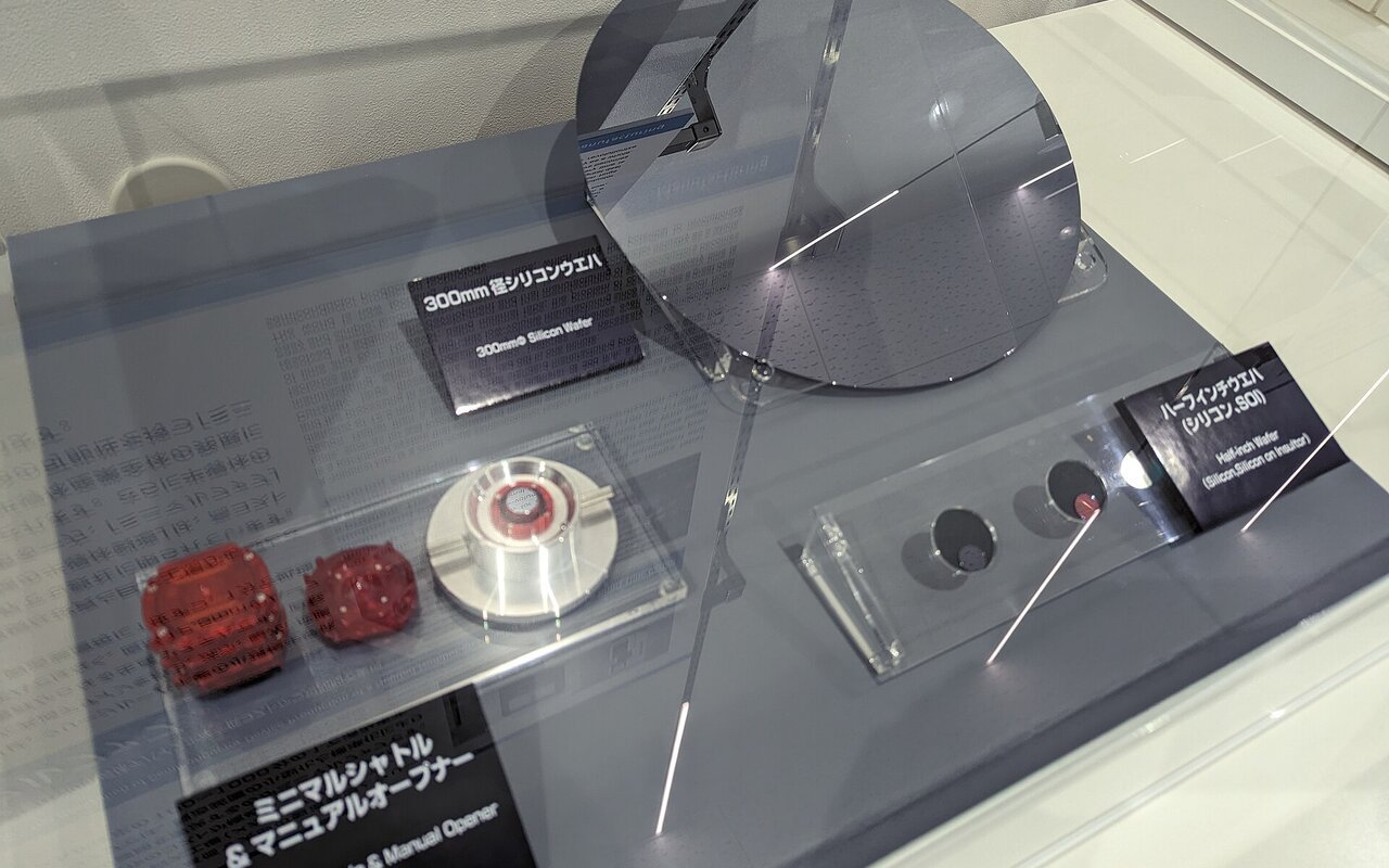 Plaquette de silicium de 300 mm de diamètre présentée dans une vitrine d'exposition, posée à la verticale à côté de petits composants électroniques et de cartels explicatifs