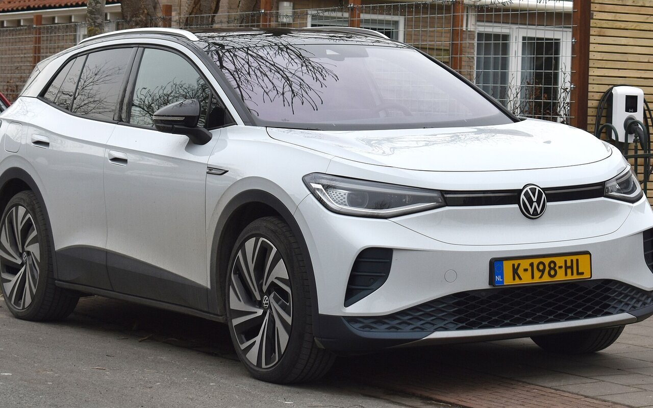 Volkswagen ID.4 Pro blanche stationnée devant une habitation, une borne de recharge murale fixée au mur derrière le véhicule