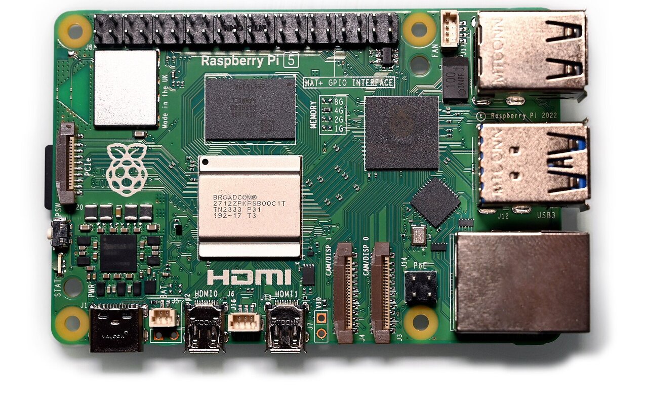 Carte Raspberry Pi 5 photographiée de dessus sur fond blanc, avec ses ports USB, son port réseau et son connecteur à broches