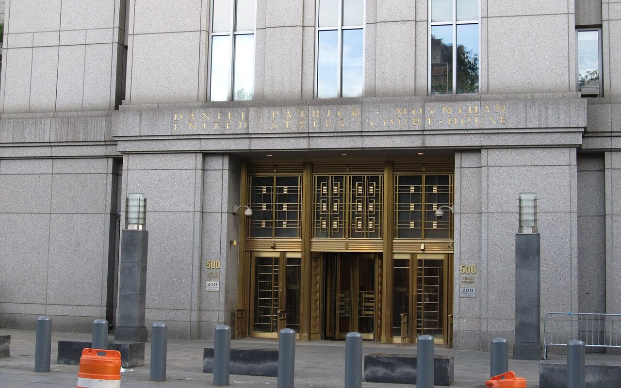 Entrée monumentale du Daniel Patrick Moynihan United States Courthouse à Manhattan : de hautes portes de bronze encadrées de piliers de pierre claire, derrière des barrières de chantier.