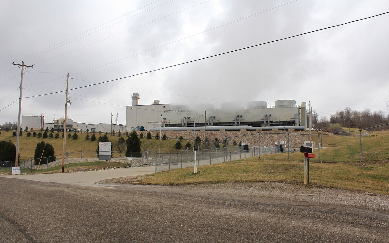Une centrale électrique au gaz naturel vue depuis une route, avec des panaches de vapeur et des lignes électriques au premier plan