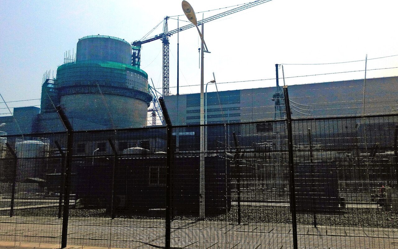 Enceinte de confinement cylindrique et grues sur le chantier de la centrale nucléaire de Sanmen, derrière une clôture grillagée