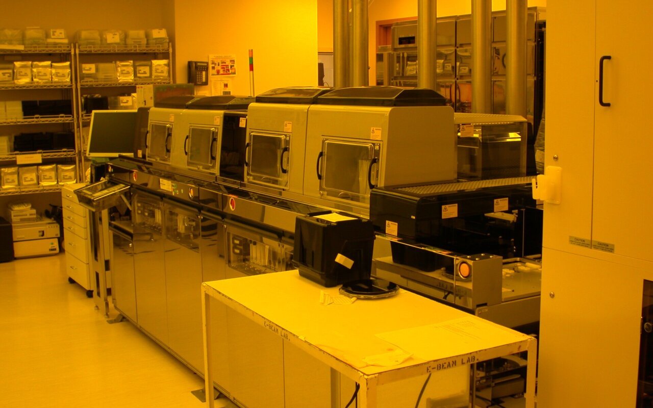 Rangée d'équipements de traitement de plaquettes de silicium dans une salle blanche de lithographie, sous l'éclairage jaune filtré caractéristique
