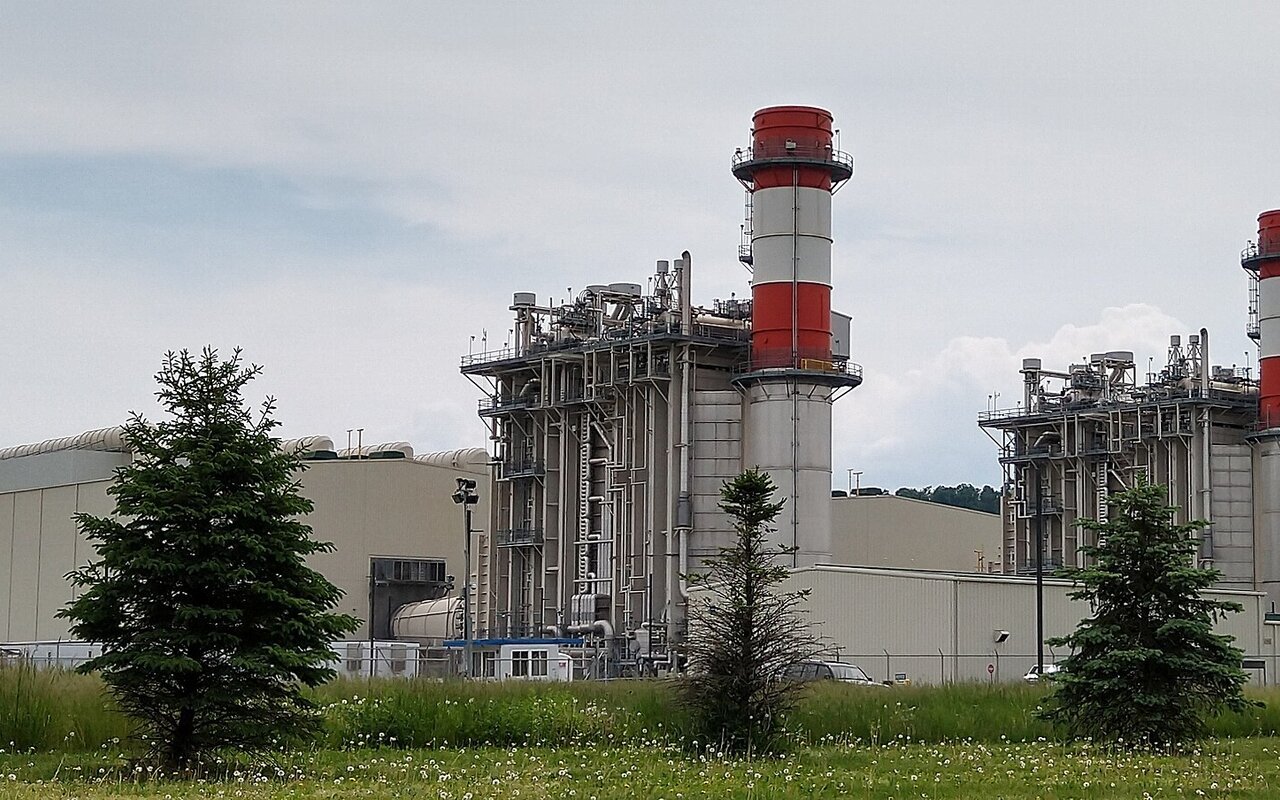Centrale électrique thermique avec deux hautes cheminées rayées de rouge et de blanc, bâtiments industriels et pelouse au premier plan