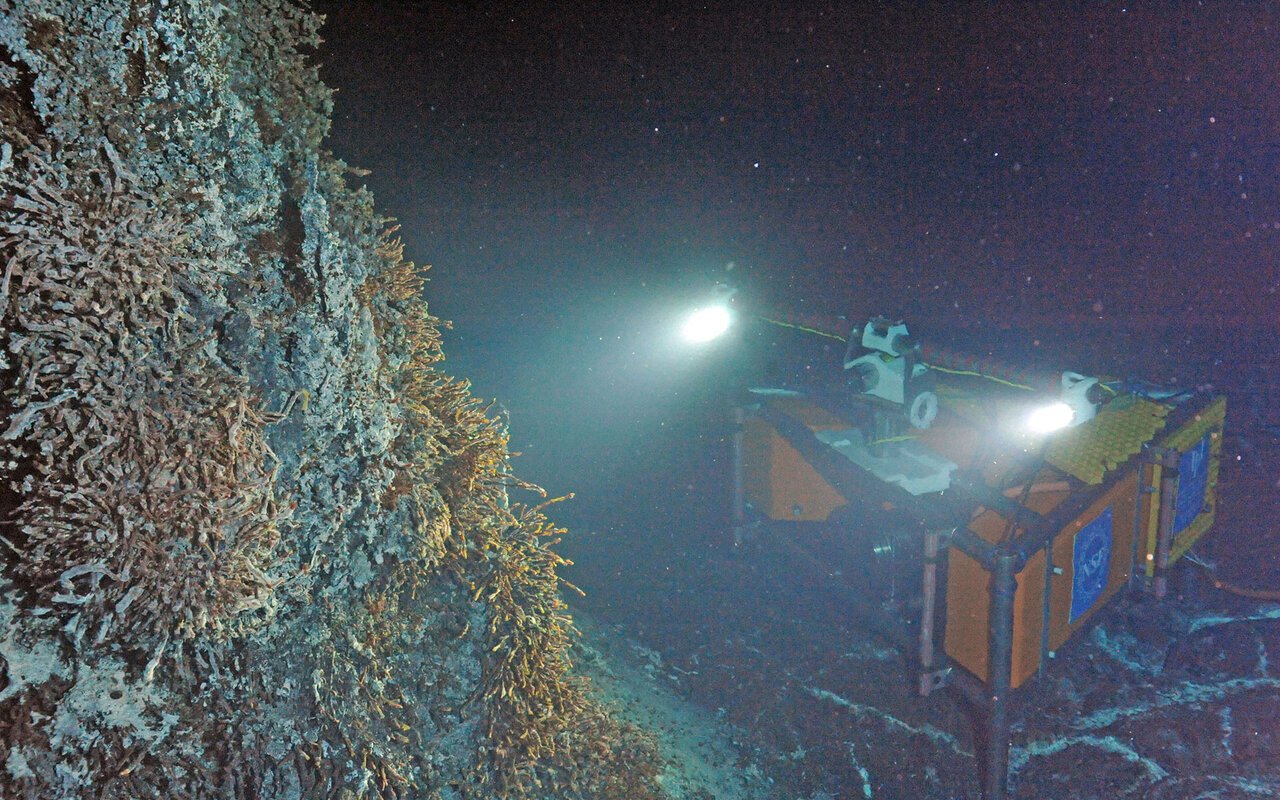 Instrument sous-marin éclairé posé au fond de l'océan à proximité d'un évent hydrothermal actif entouré de faune