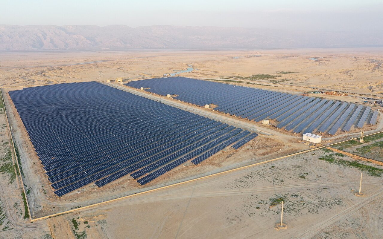 Vue aérienne d'une grande centrale photovoltaïque au sol installée en plein désert, rangées de panneaux alignées sur un sol sableux