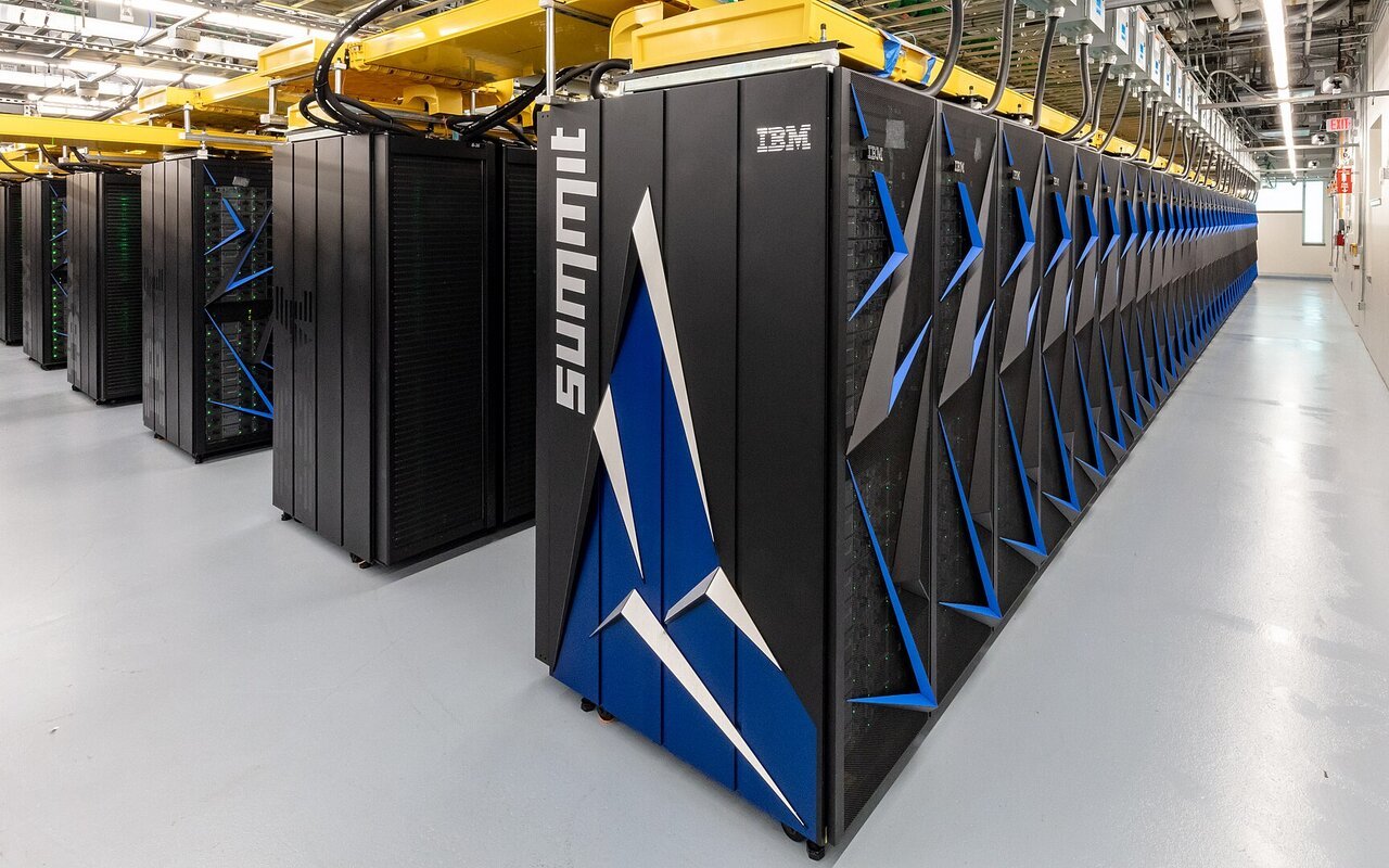 Longue rangée d'armoires informatiques noires du supercalculateur Summit dans une salle machine, avec un chemin de câbles jaune au plafond