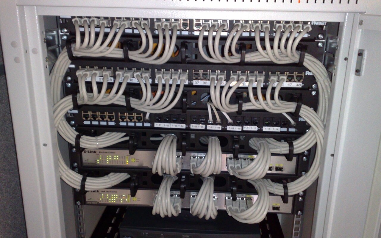 Baie informatique de 19 pouces contenant des commutateurs Ethernet et des panneaux de brassage reliés par des cordons gris